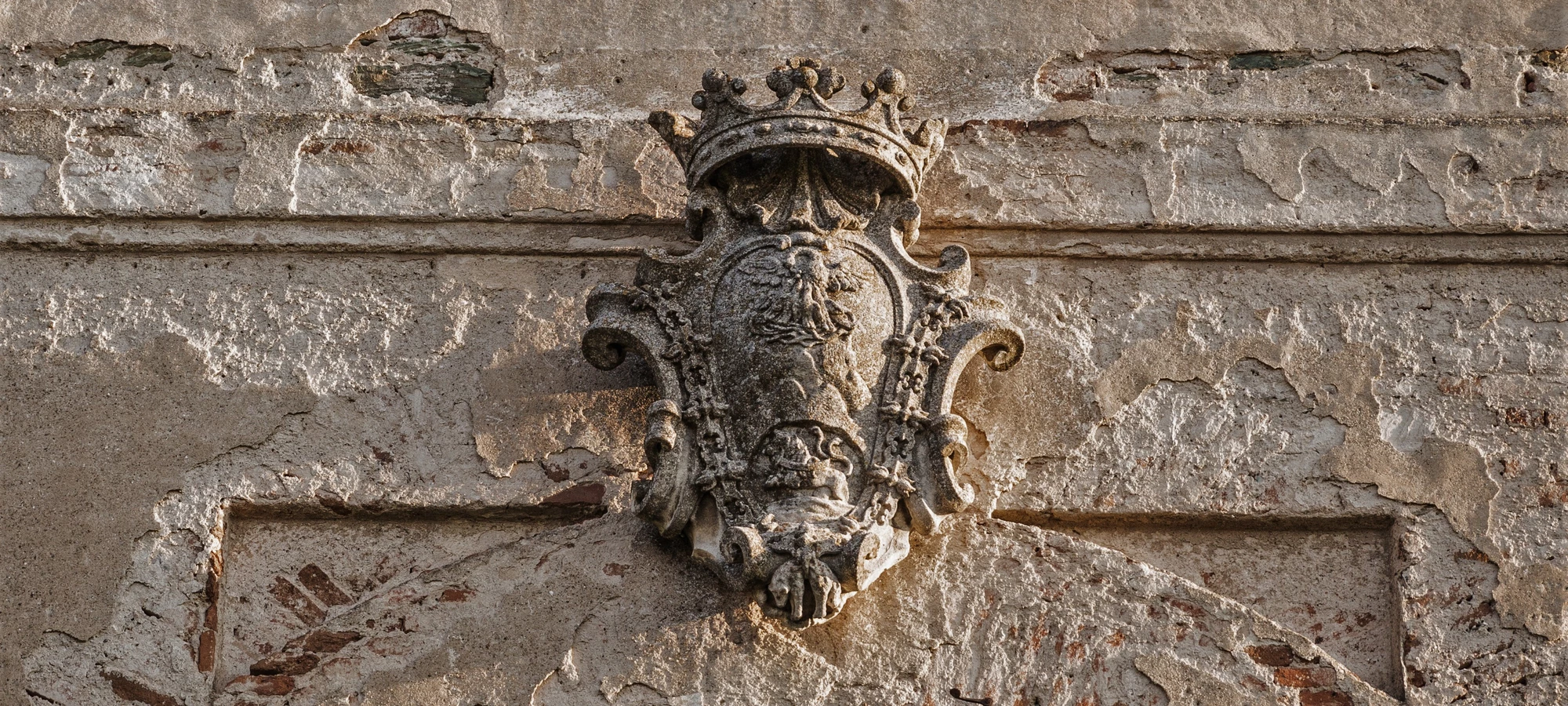 Steinernes Wappen vor verwitterter Mauer