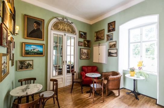 Eine grüne Wand mit Bildern, zwei Sitzecken mit Kaffeehaustischchen