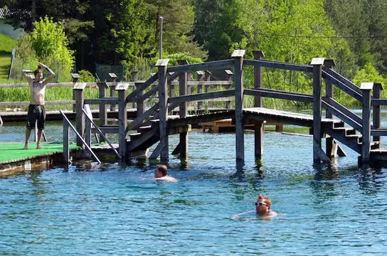 Schwimmende Leute im Badeteich vor einem Holzsteg